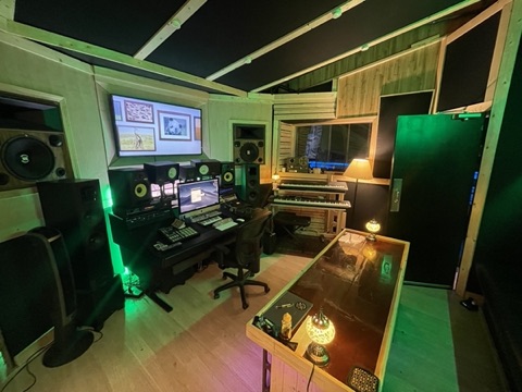 Control room mixing desk with studio monitors, MIDI keyboards, and a wall-mounted screen
