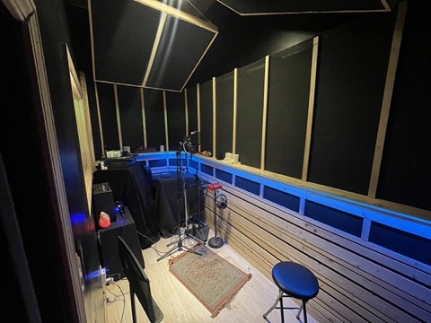Vocal booth with mic stands, headphones, and a rug, lit in blue
